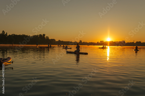 Silhouettes of a people on a sup on the background of the river in the rays of the sunset