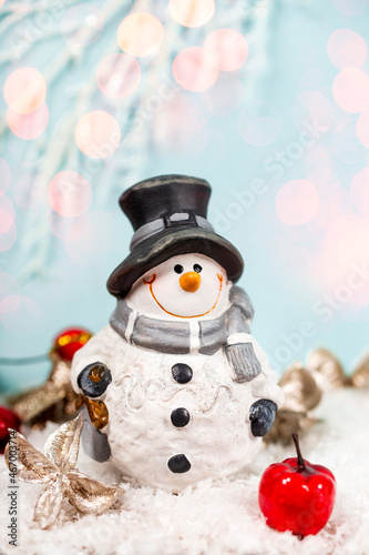 Festive New Year vertical card. Snowman and Christmas decorations in a snow on a light blue background