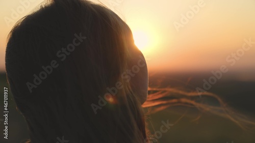 girl prays looking at sunset, long hair is flying away in glare of sunlight rays in strong wind, looking at dawn, lonely hike of brave girl, looking into sky with her eyes, believing good