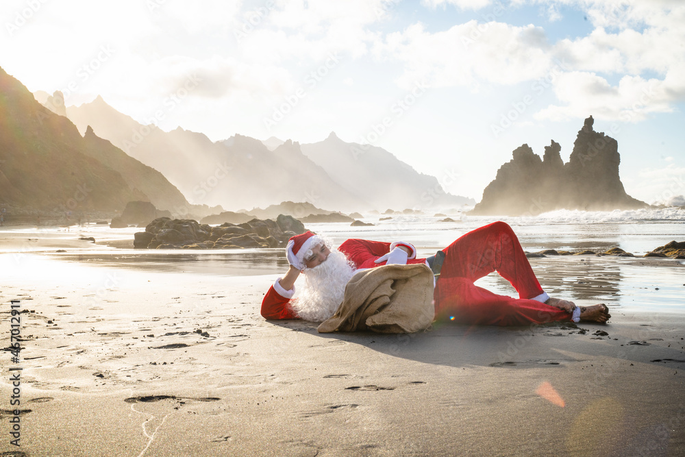 Obraz premium Funny conceptual photo of Santa Claus lying and relaxing on tropical beach at the ocean.