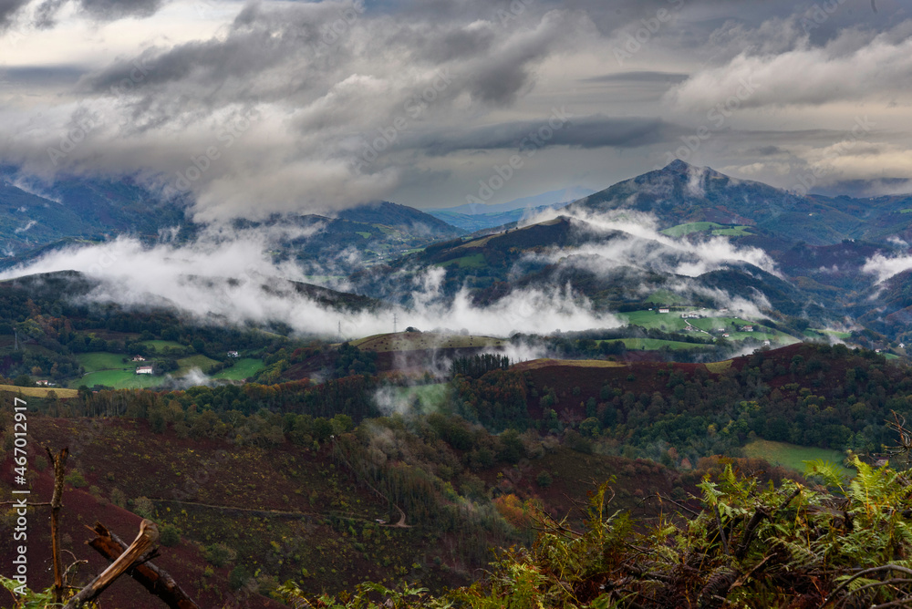 Landscape of green and brown winter mountains full of low white clouds stuck to the ground. Completely cloudy dark sky, dark gray, on a rainy autumn morning. In the background the valley.