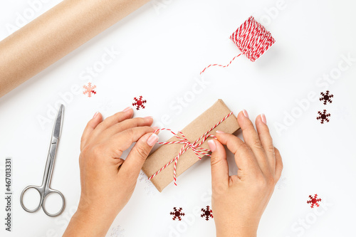 flat lay female hands tie bow from red festive rope on Christmas gift box with decor of red snowflakes on white isolated background.  photo