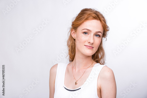 Portrait of a beautiful young woman of European, Caucasian nationality with long red hair and freckles on her face posing on a white background in the studio. Close-up student girl in a white blouse