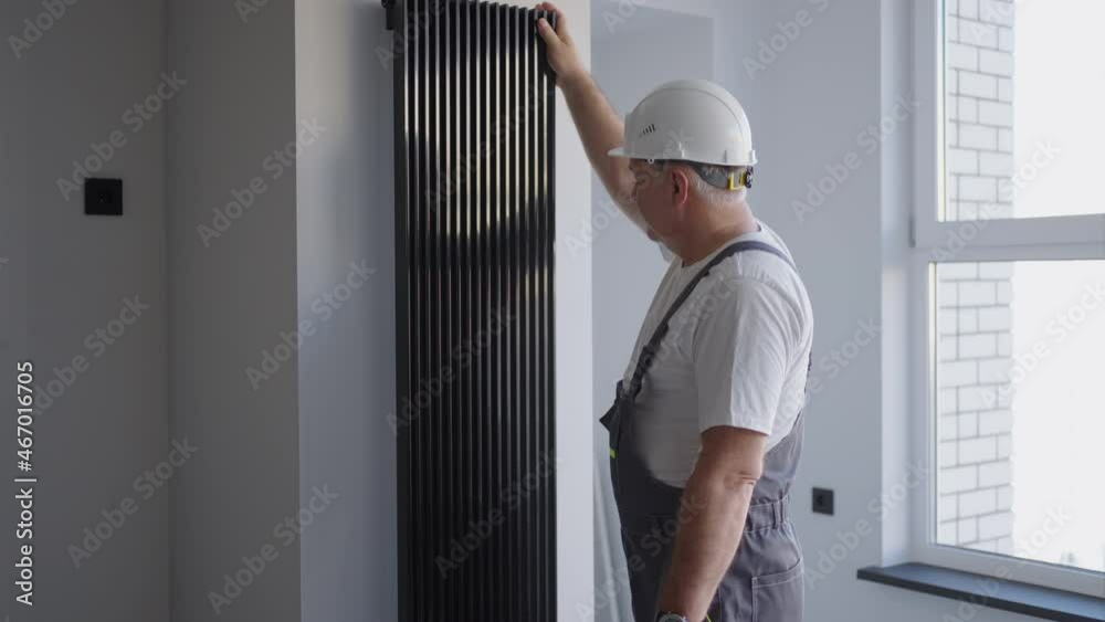 A man plumber in a helmet checks modern batteries for heat output and heating system. Heating season A man plumber in a helmet checks modern batteries for heat output and heating system. Heating season