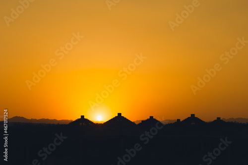 Majestic dusk in tropics. Goden sunset sky with beautiful silhouette roofs beach umbrellas and mountains in the evening. Warm orange colors. Abstract nature and travel background. Egypt summer.