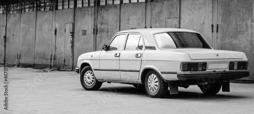 Photo of old car standing before rusty gate of building, black and white