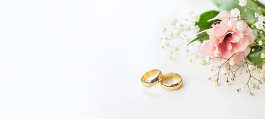 Pink flowers and two golden wedding rings on white background.