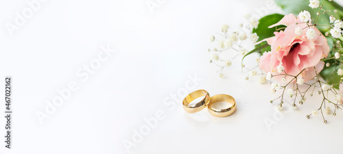 Pink flowers and two golden wedding rings on white background. photo