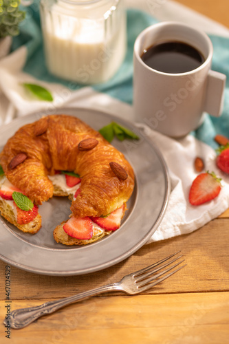 One mouth-watering croissant with butter  slices of fresh strawberries  mint leaves  sprinkled with almonds and a cup of aromatic black coffee. Classic French breakfast. Restaurant  cafe  hotel.