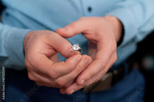 A ring made of white gold and with a precious stone in the hand of a man in a blue shirt