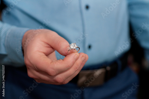A ring made of white gold and with a precious stone in the hand of a man in a blue shirt