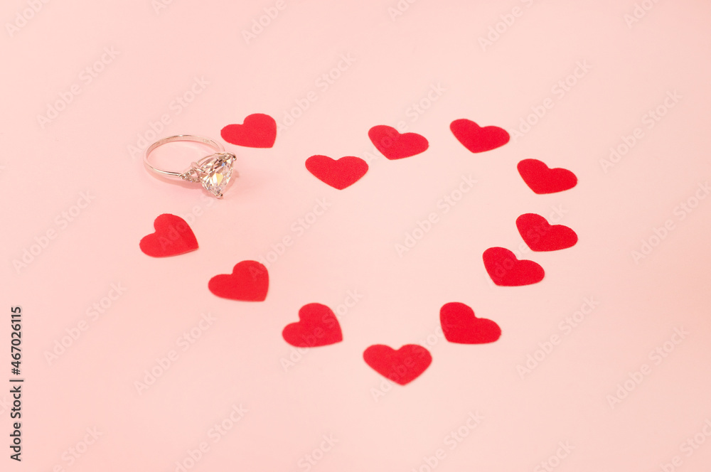 white gold ring with a precious stone on a pink background with confetti in the form of hearts