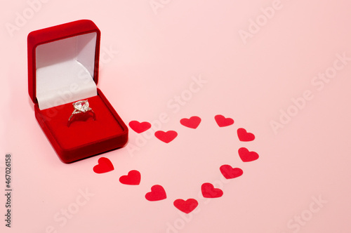 white gold ring with a precious stone in a red box on a pink background with confetti in the form of a heart © Яна Скиданенко