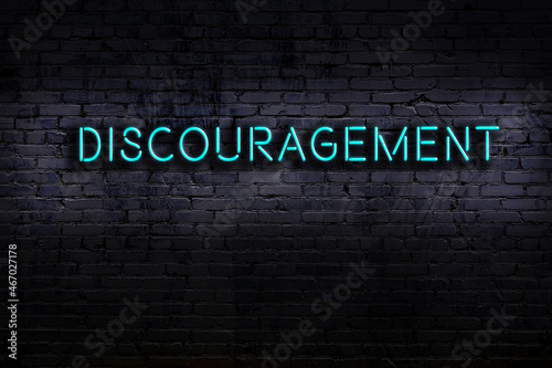 Neon sign. Word discouragement against brick wall. Night view