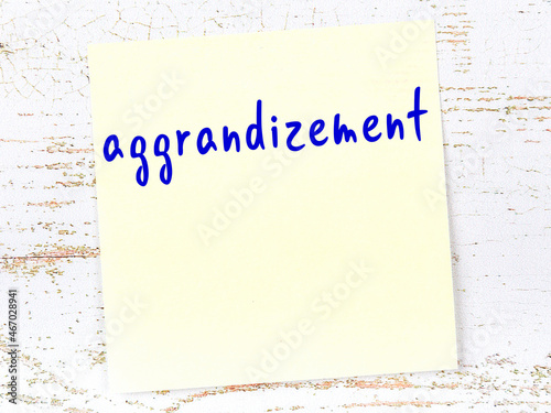 Yellow sticky note on wooden wall with handwritten word aggrandizement