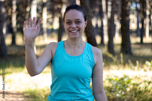portrait of a young sporty girl in sportswear in nature waving to the camera