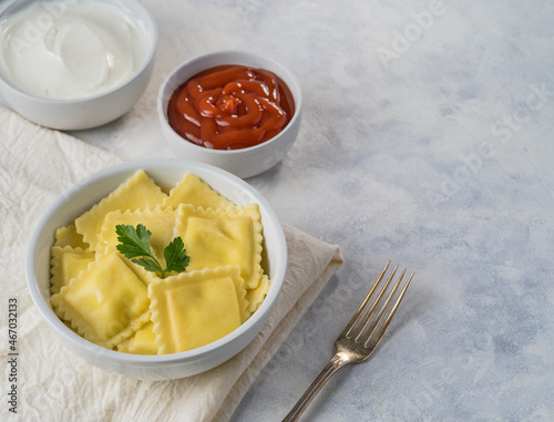 A portion of classic Italian ravioli and two gravy - tomato and sour cream. There is a fork nearby. White background. No people. Restaurant, hotel, cafe, cookbook, culinary blog.