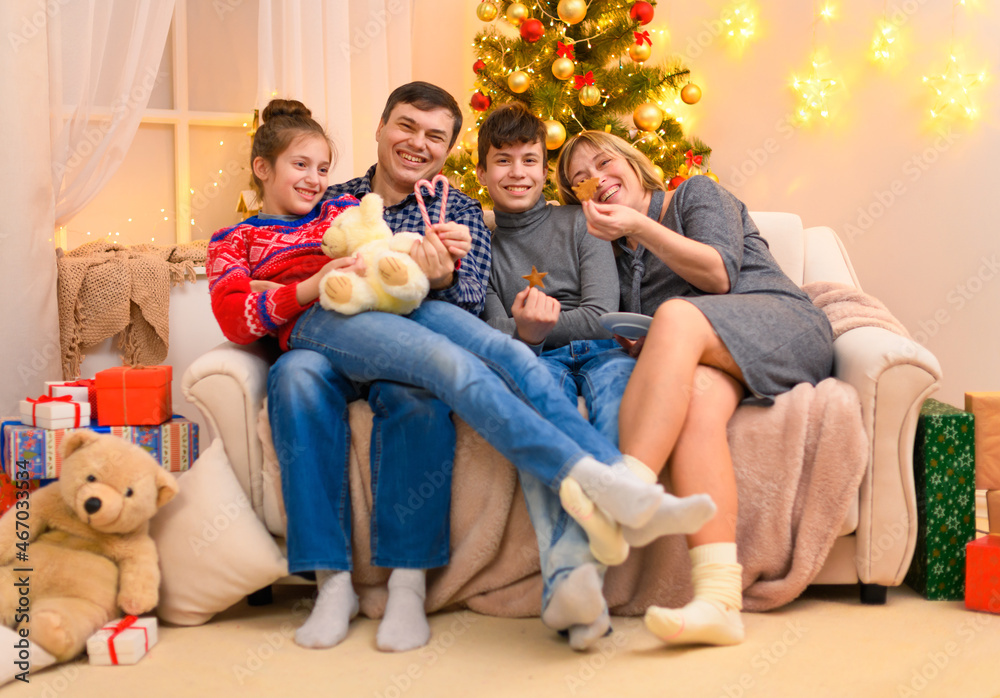 Winter holiday concept - Family sitting on a couch and posing in new year or christmas decoration. Children and parents. Holiday lights and gifts, Christmas tree decorated with toys.