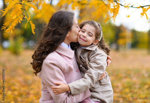 Mother and daughter portrait in an autumn park. Happy people pose against the background of beautiful yellow trees. They hug and are happy together.