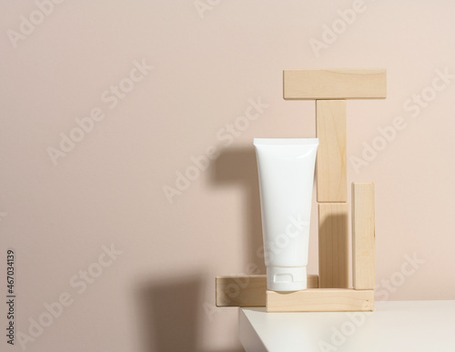 empty white plastic tubes for cosmetics on a beige background with wooden blocks. Packaging for cream, gel, serum, advertising and product promotion, mock up