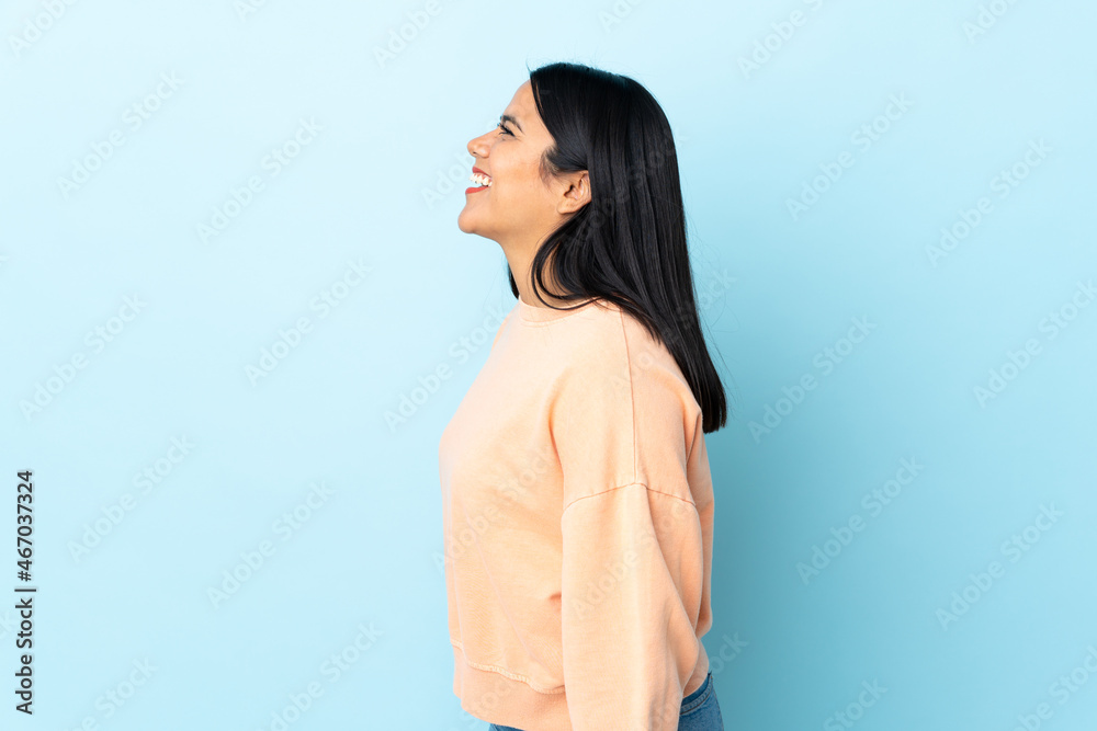 Young latin woman woman isolated on blue background laughing in lateral position Young latin woman woman isolated on blue background laughing in lateral position