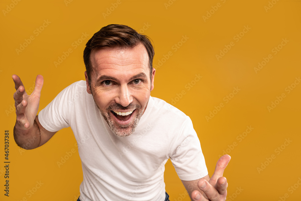 Funny handsome man with crazy facial expression standing in front of camera against yellow studio background while making fun, smiling Funny handsome man with crazy facial expression standing in front of camera against yellow studio background while making fun, smiling