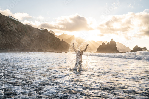 Man splashing water during summer holidays , having fun on a tropical Benijo beach at sunset photo