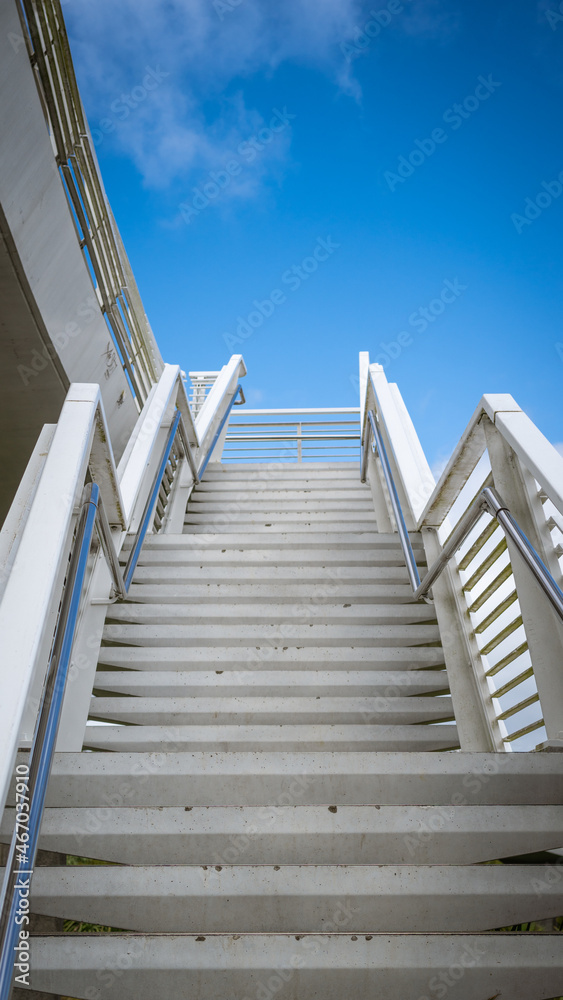 Fototapeta premium Background Architecture White Stairs Ascending to a Bridge up to Bright Blue Sky Vertical with Copy Space