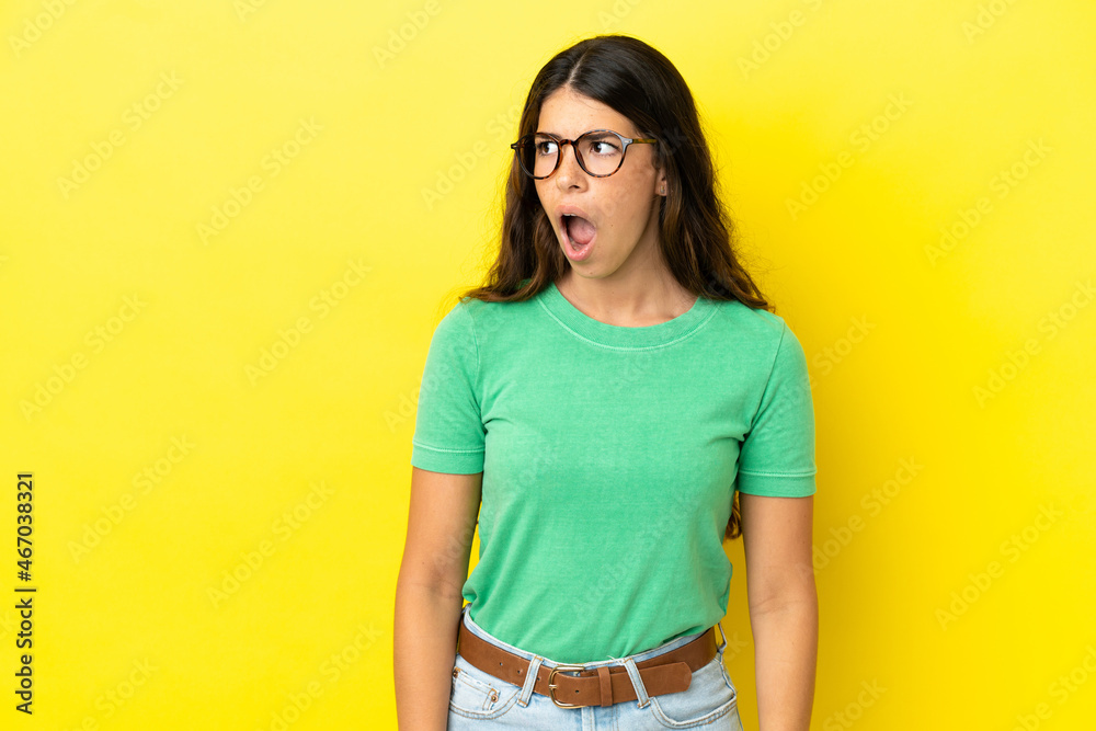 Young caucasian woman isolated on yellow background doing surprise gesture while looking to the side Young caucasian woman isolated on yellow background doing surprise gesture while looking to the side