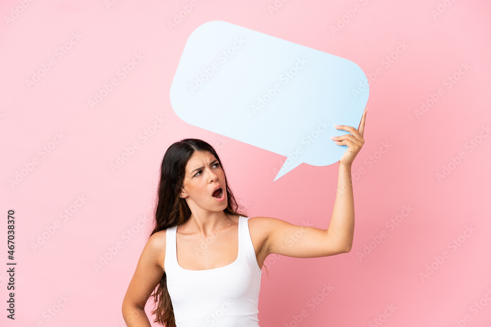 Young caucasian woman isolated on pink background holding an empty speech bubble and with sad expression