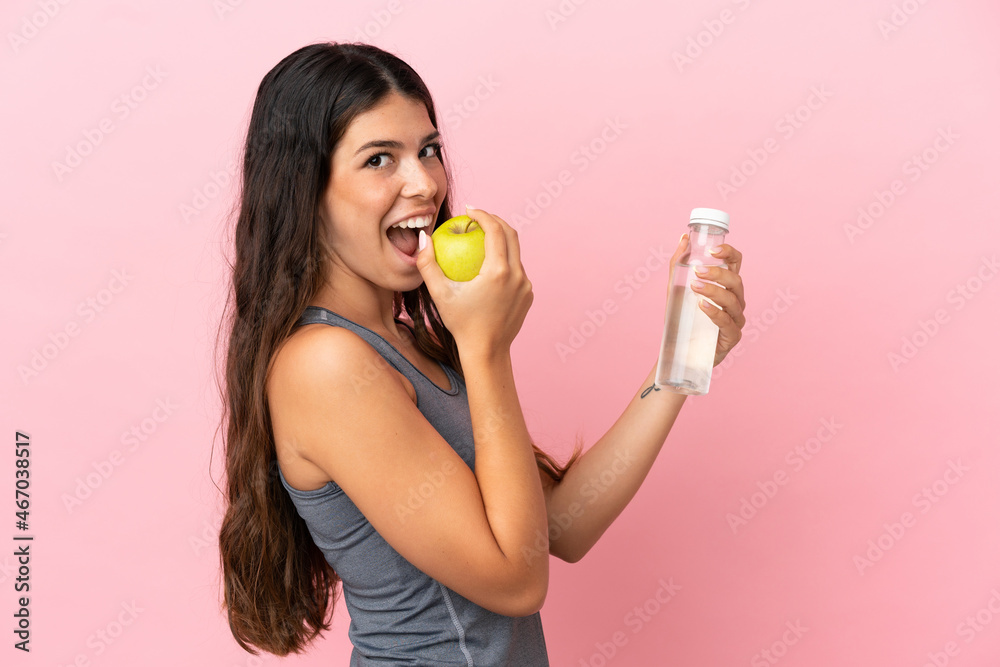 Young caucasian woman isolated on pink background with an apple and with a bottle of water Young caucasian woman isolated on pink background with an apple and with a bottle of water