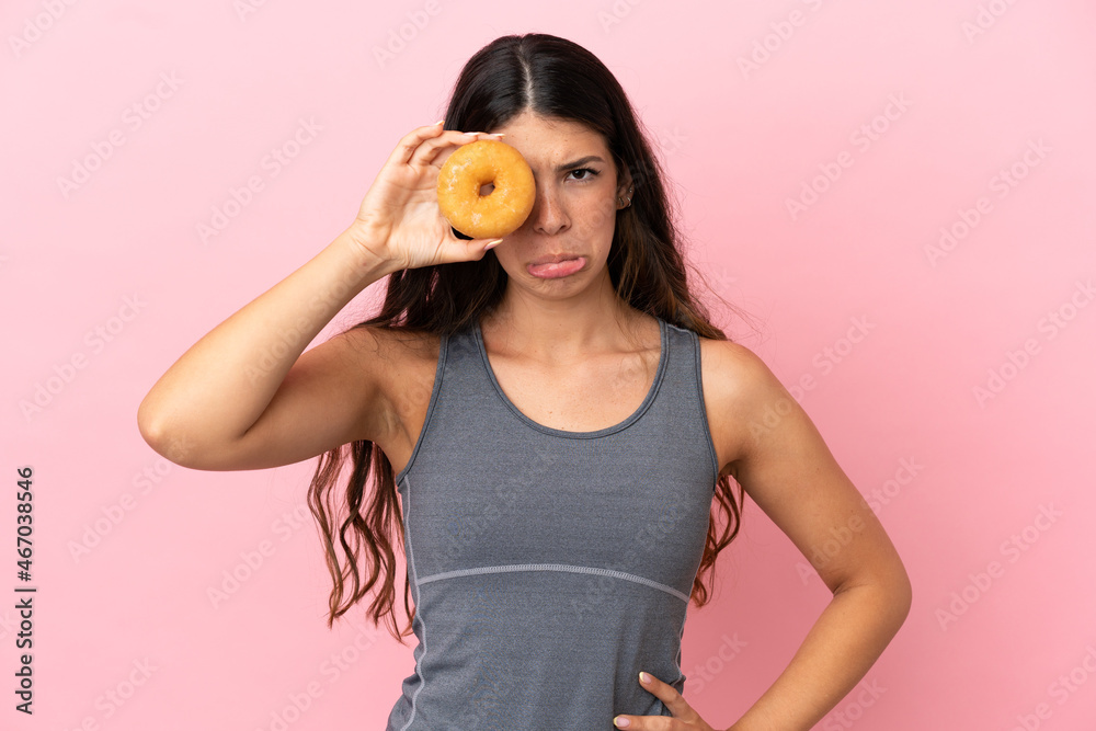 Young caucasian woman isolated on pink background holding donuts in eyes with sad expression Young caucasian woman isolated on pink background holding donuts in eyes with sad expression