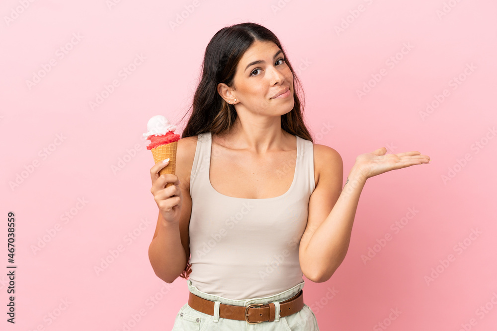Young caucasian woman with a cornet ice cream isolated on pink background having doubts while raising hands Young caucasian woman with a cornet ice cream isolated on pink background having doubts while raising hands