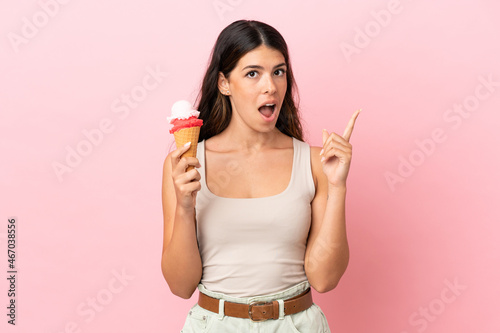Young caucasian woman with a cornet ice cream isolated on pink background thinking an idea pointing the finger up
