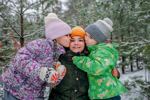 Kids with mom enjoy first snow in winter forest and have fun together, active winter weekend, seasonal outdoor activities, happy family lifestyle