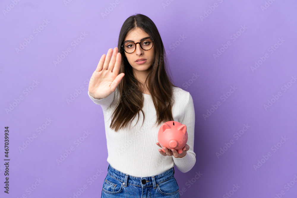 Young caucasian woman holding a piggybank isolated on purple background making stop gesture Young caucasian woman holding a piggybank isolated on purple background making stop gesture