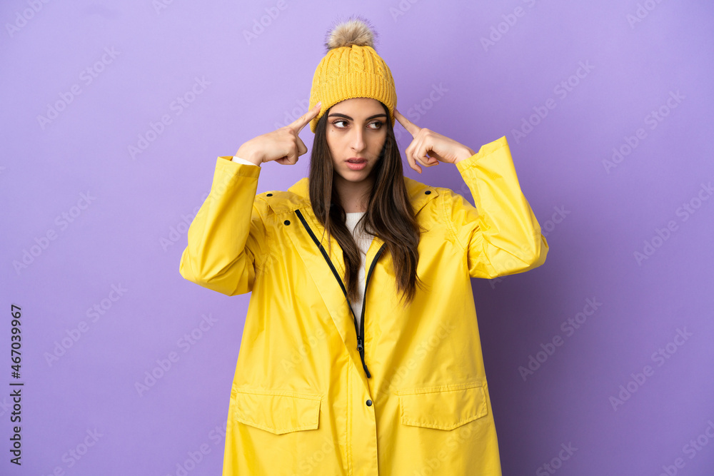 Young caucasian woman wearing a rainproof coat isolated on purple background having doubts and thinking Young caucasian woman wearing a rainproof coat isolated on purple background having doubts and thinking