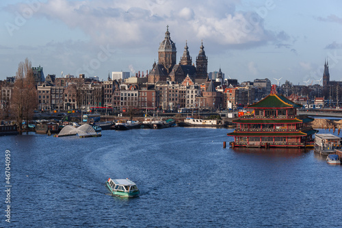 Passenger boat crosses the Amsterdam river against the backgound of historical church and famous floating Chinese restaurant, Netherlands. The beautiful winter weather.