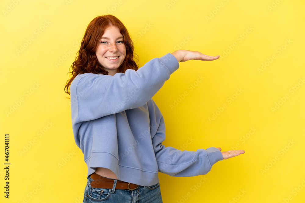 Teenager reddish woman isolated on yellow background holding copyspace to insert an ad Teenager reddish woman isolated on yellow background holding copyspace to insert an ad