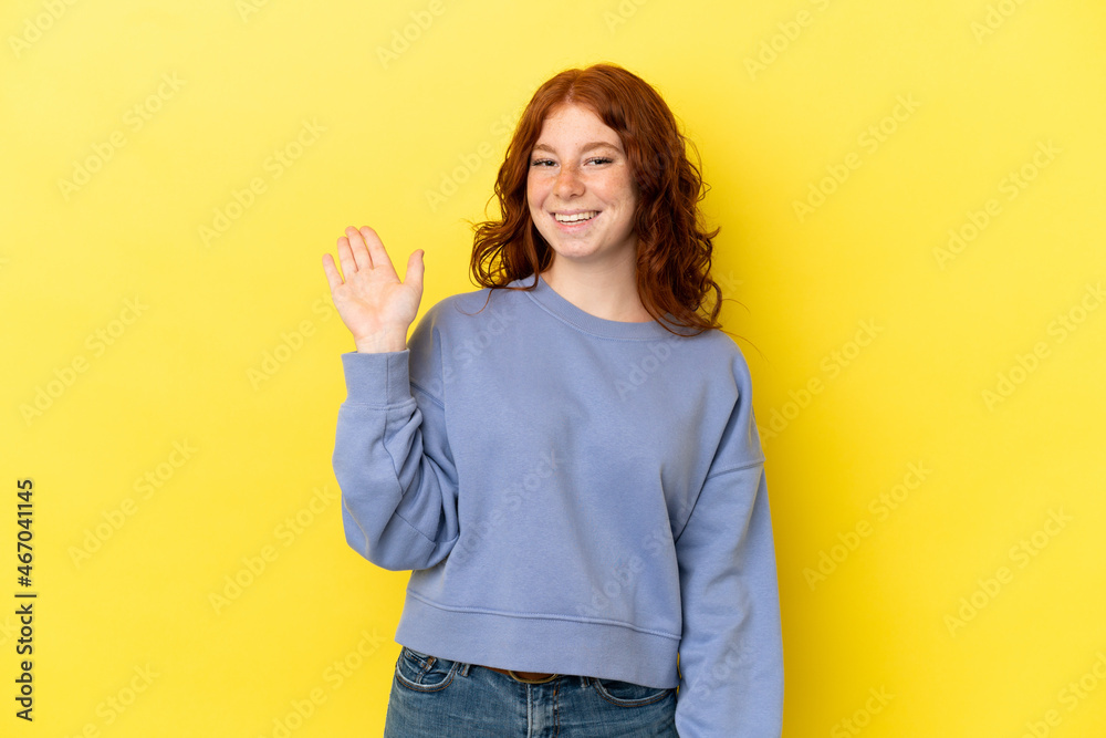 Teenager reddish woman isolated on yellow background saluting with hand with happy expression Teenager reddish woman isolated on yellow background saluting with hand with happy expression