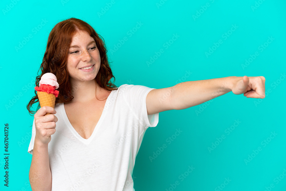 Teenager reddish woman with a cornet ice cream isolated on blue background giving a thumbs up gesture Teenager reddish woman with a cornet ice cream isolated on blue background giving a thumbs up gesture