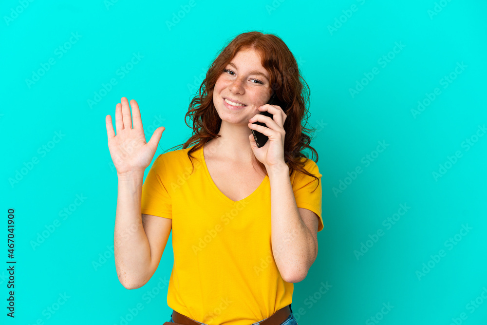 Teenager reddish woman using mobile phone isolated on blue background saluting with hand with happy expression Teenager reddish woman using mobile phone isolated on blue background saluting with hand with happy expression