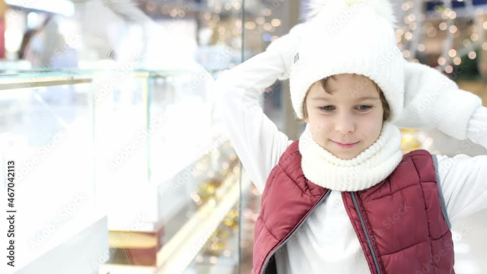 Boys in Santas hat looks into the store through the window in market. glowing lights on the background. Boys in Santas hat looks into the store through the window in market. glowing lights on the background.