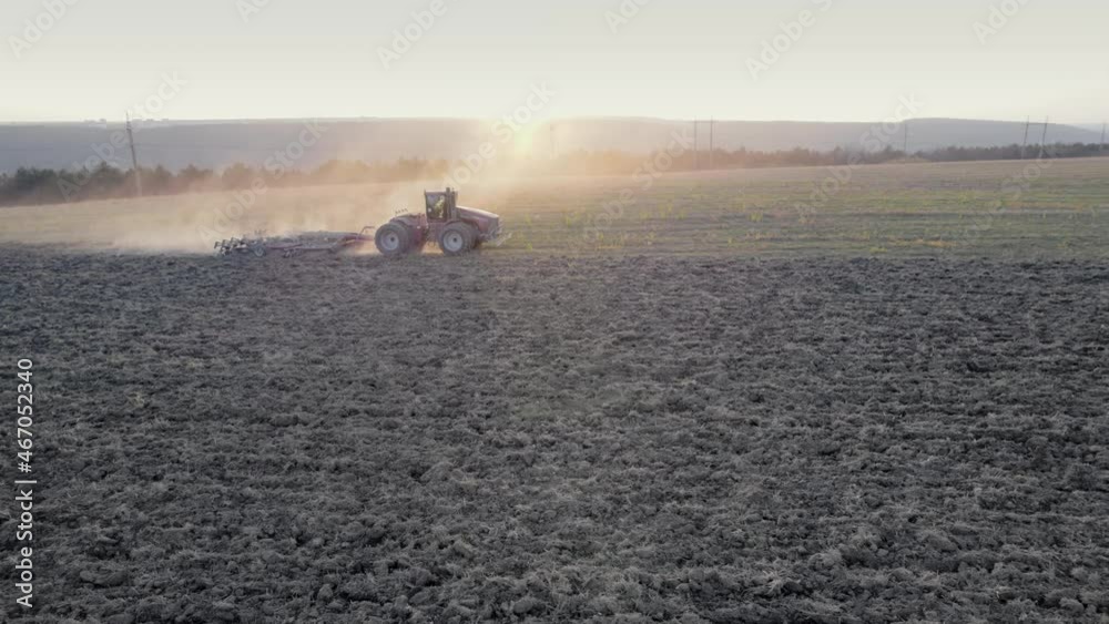 Drone tracking shot of farming tractor plowing dry field after