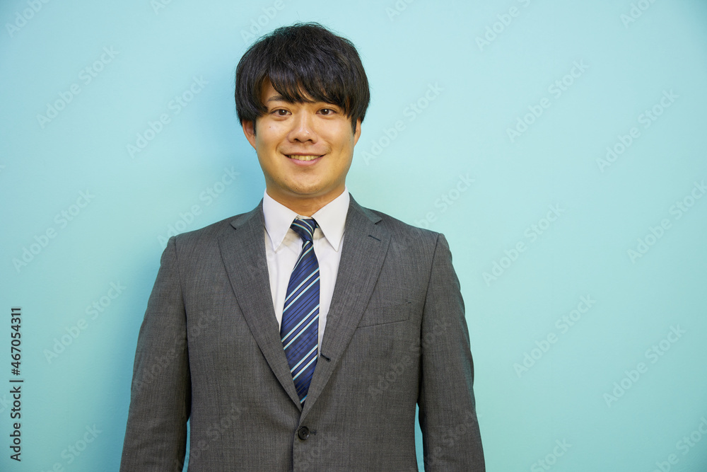 青背景の前で爽やかに笑うスーツを着た日本人男性 青背景の前で爽やかに笑うスーツを着た日本人男性