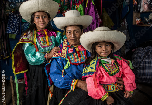 Mujer madre latinoamericana andina haciendo hilo de lana de oveja y enseñando el telar de cintura a sus hijas.