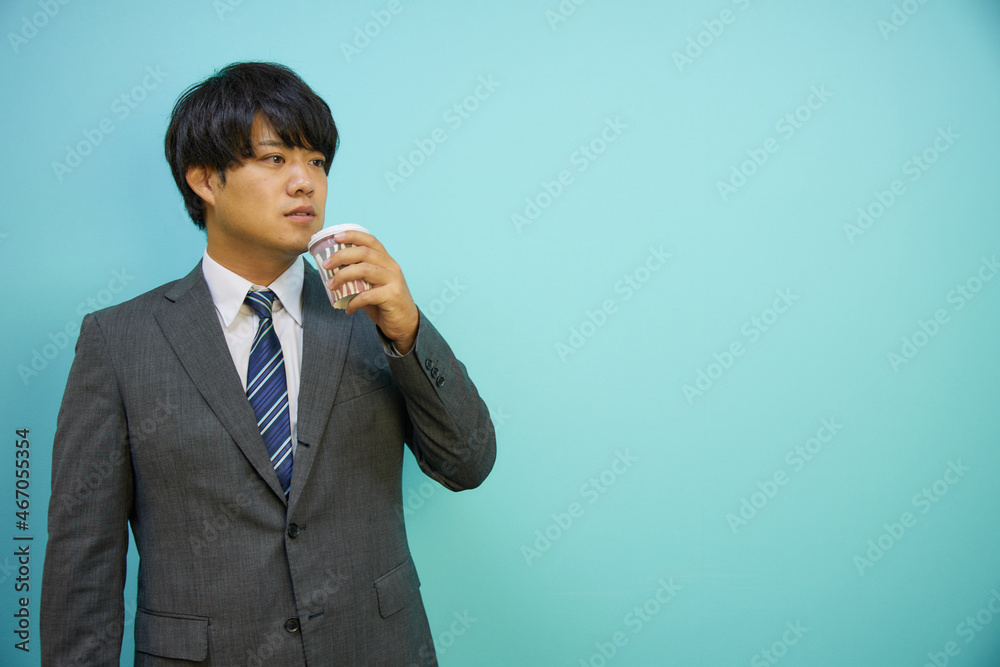 青背景の前でコーヒーカップを持つビジネスマン男性