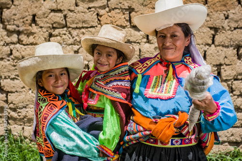 Mujer madre latinoamericana andina haciendo hilo de lana de oveja y enseñando el telar de cintura a sus hijas. photo