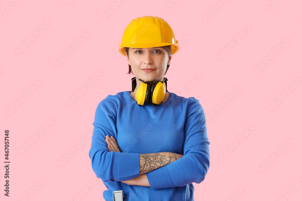 Female construction worker with hardhat and ear protectors on pink background Female construction worker with hardhat and ear protectors on pink background