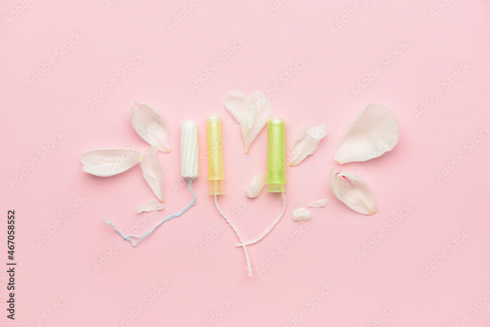 Menstrual tampons and flower petals on pink background